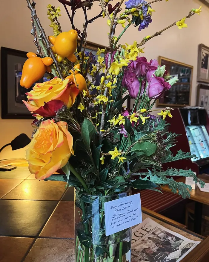 Anniversary flowers with a card reading Happy Anniversary Chez Lucien, 20 Years, thank you to all our wonderful customers and staff
